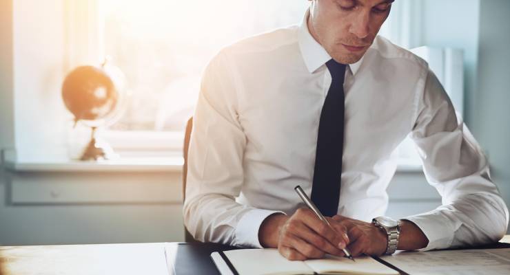 Close up of business man in shirt and tie working in his office writing in a classic note book